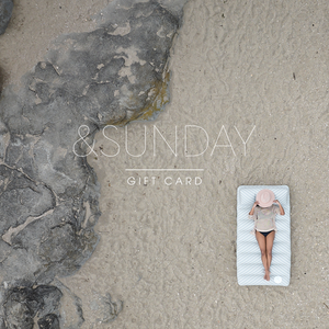 Person lying on a mat in the sand with 'SUNDAY' branding.