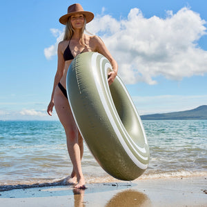 Woman holding a large inflatable ring on a beach with ocean and sky in the background